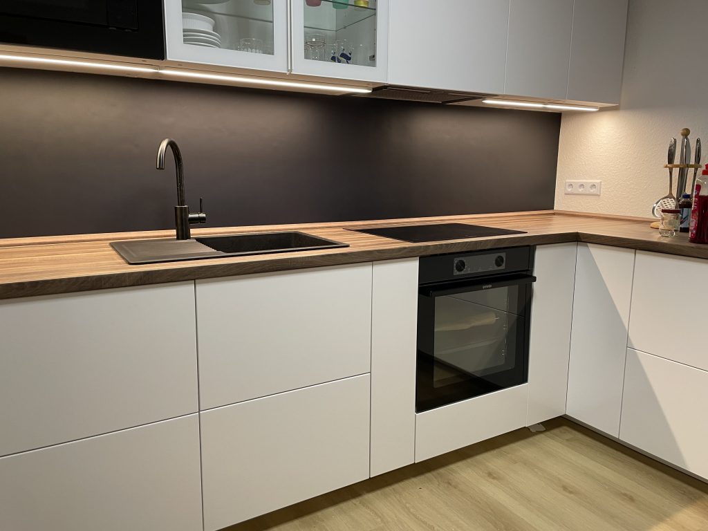 Moderne L-förmige Küche mit weißen Schränken, schwarzer Küchenrückwand, Holzarbeitsplatte, schwarzer Spüle Herd und Backofen.