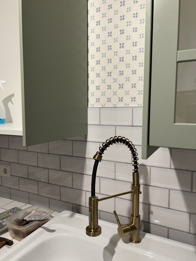 Eine grüne Küche mit einem goldenen Wasserhahn und einem weißen Fliesenspiegel.