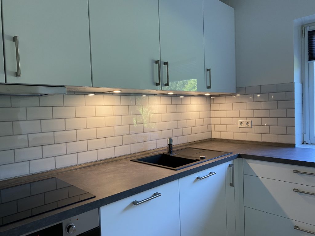 Eine weiße Küche mit dunkler Arbeitsfläche aus Holz und einem weißen Fliesenspiegel.