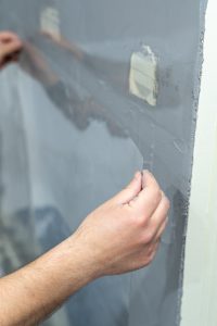 Hand legt transparente Schutzfolie auf einer Wand mit Putz an