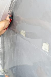 Hand streicht transparente Schutzfolie mit Rakel auf Putz Wand