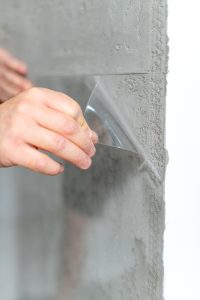 Hand zieht transparente Schutzfolie von einer rauen Betonoberfläche ab