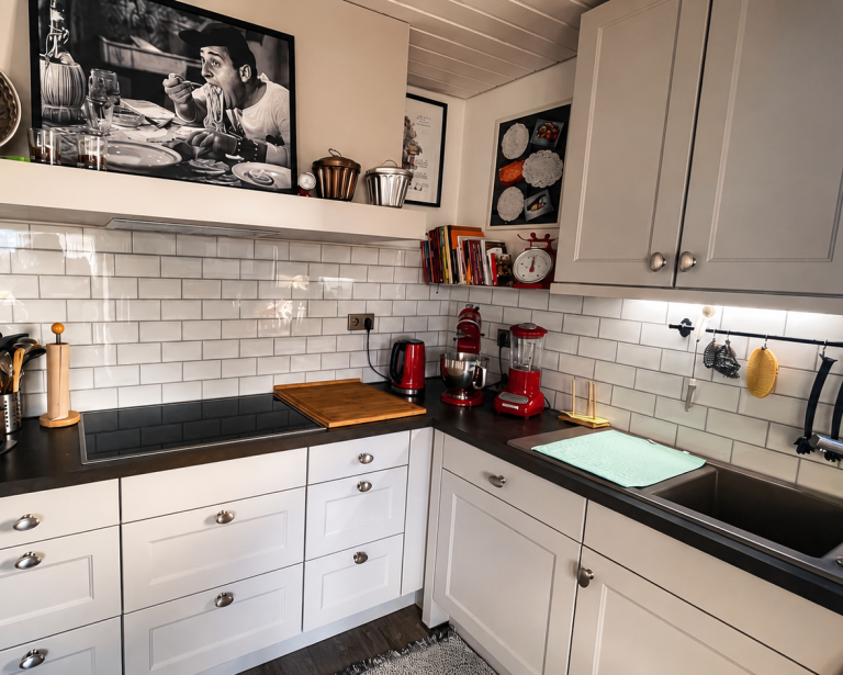 Küche mit weiß gekachelter Wand. Roten Küchengeräten, schwarzen Arbeitsflächen und weißen Schränken.