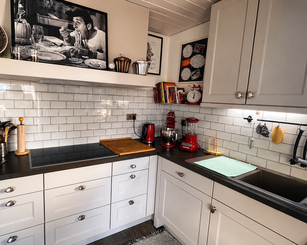Küche mit weiß gekachelter Wand. Roten Küchengeräten, schwarzen Arbeitsflächen und weißen Schränken.
